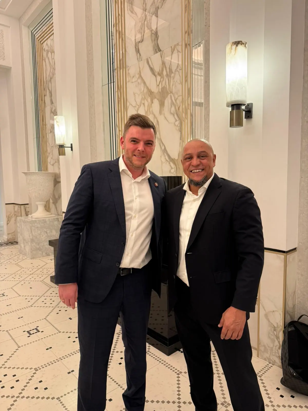 Filipp Sviridenko and Roberto Carlos smiling in a marble hotel lobby