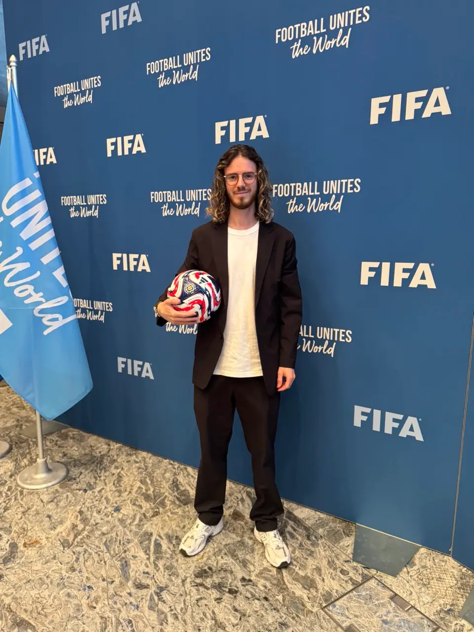 Marks Amosejevs holding a football in front of a branded backdrop