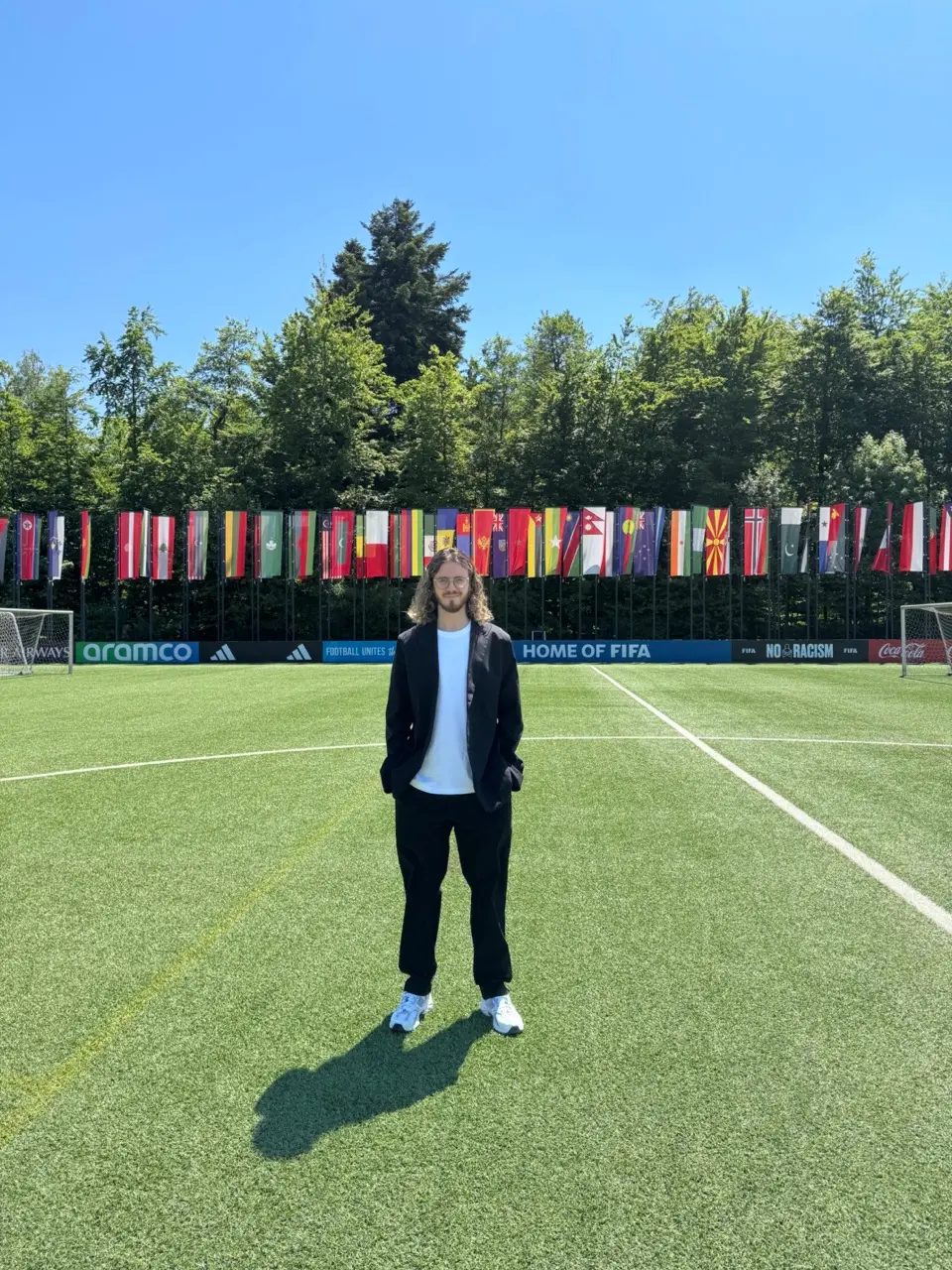 Marks Amosejevs standing on a pitch in front of a line of national flags