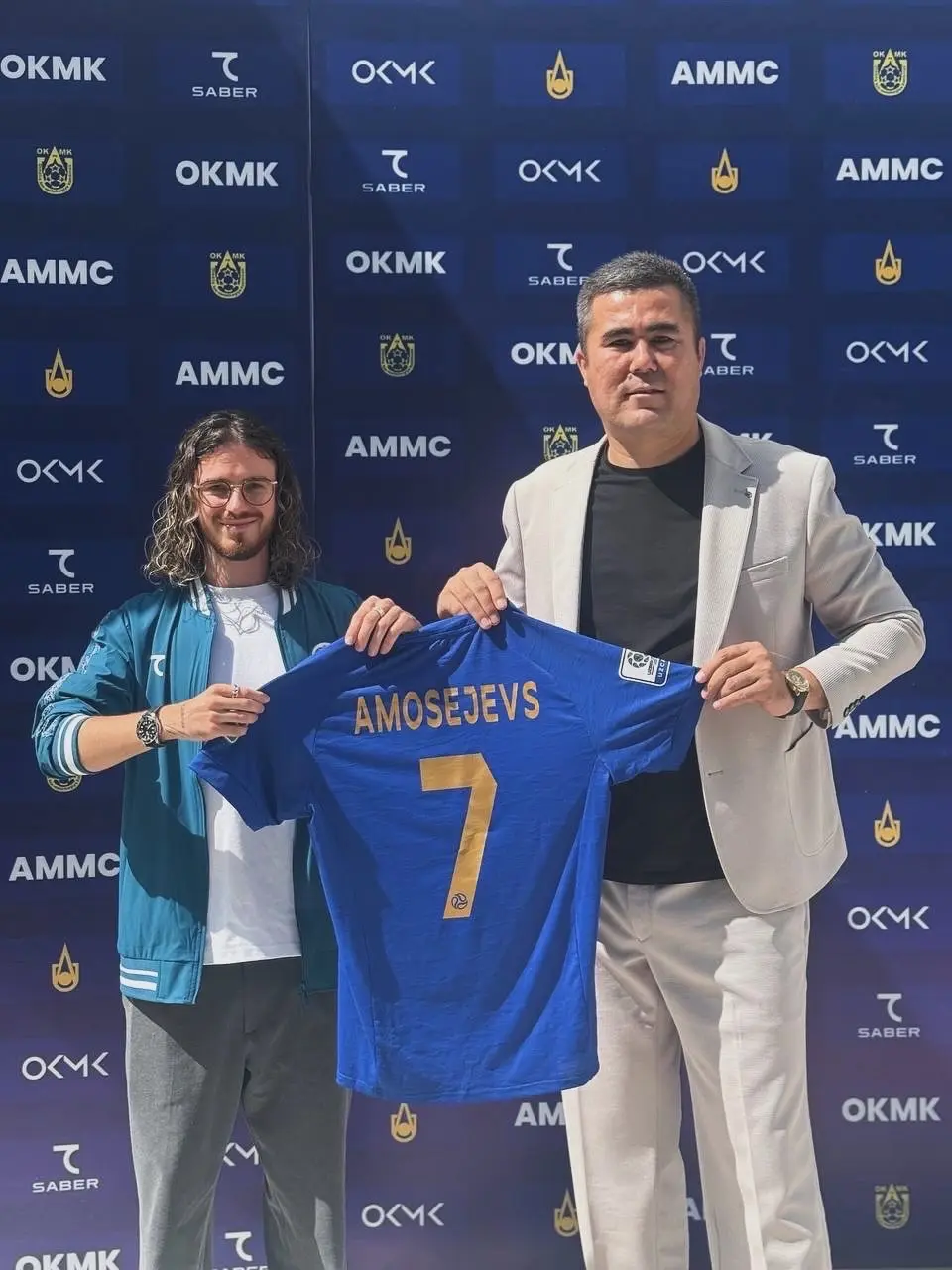 Marks Amosejevs and a club official holding a shirt printed with his name